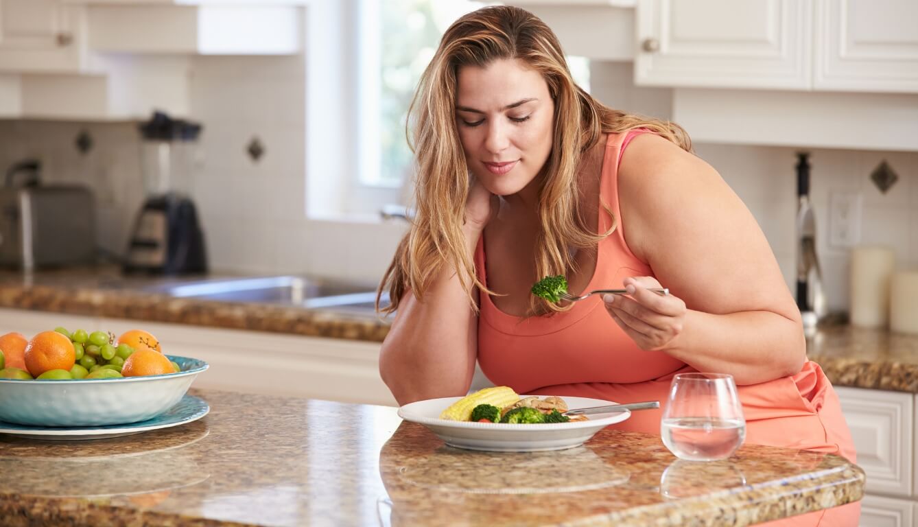 Overweight Woman Eating Healthy Meal In Kitchen   