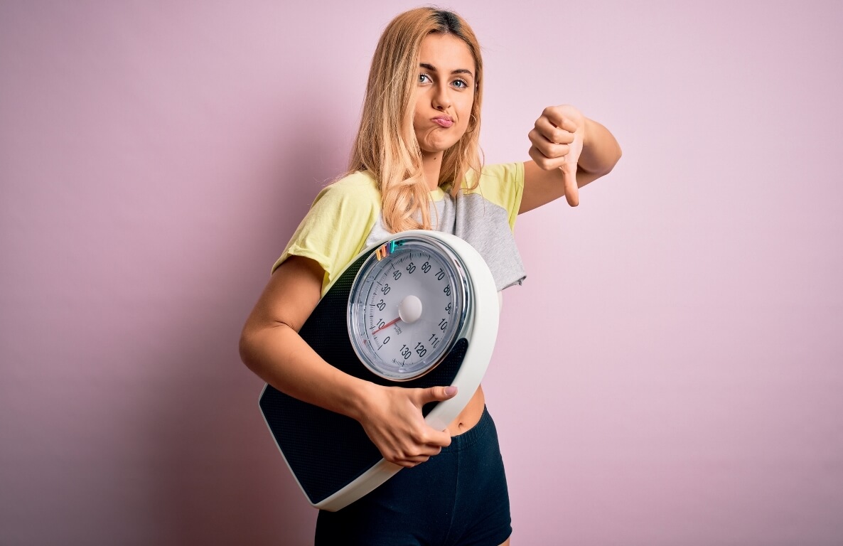 woman on diet holding weight machine with thumbs down