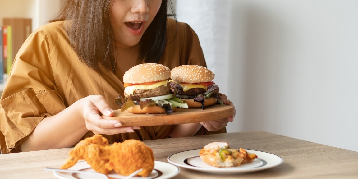 Hungry overweight woman holding hamburger on wooden plate