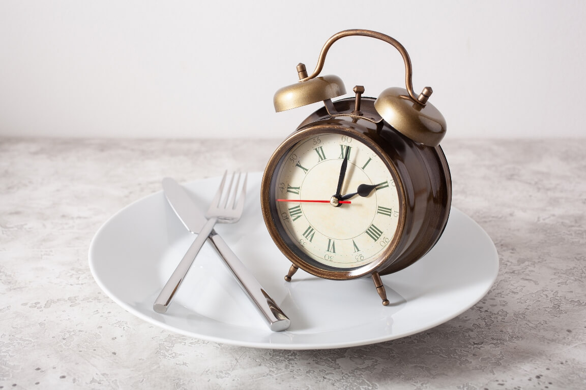 Intermittent fasting, fork and knife crossed and alarmclock on plate