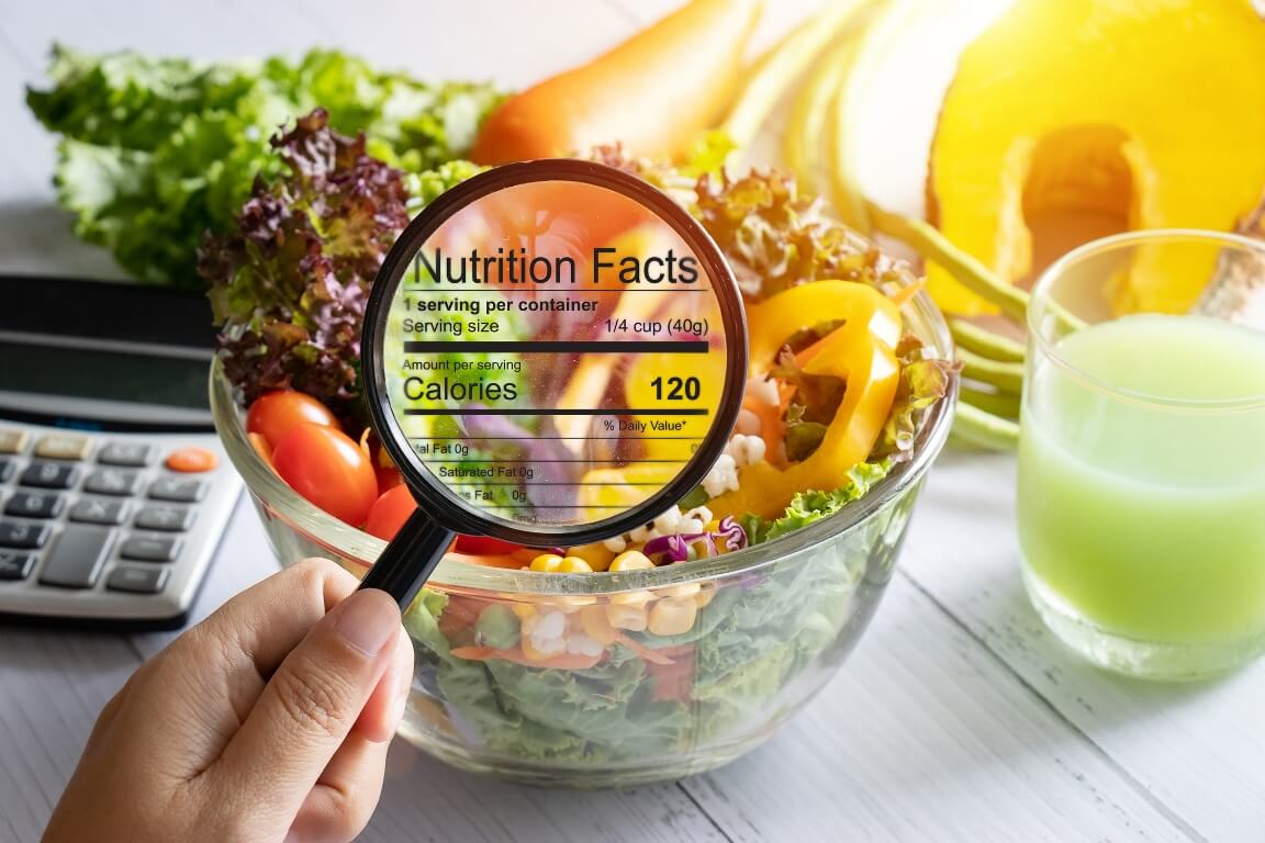 Nutritional information concept. hand use the magnifying glass to zoom in to see the details of the nutrition facts from food , salad bowl 