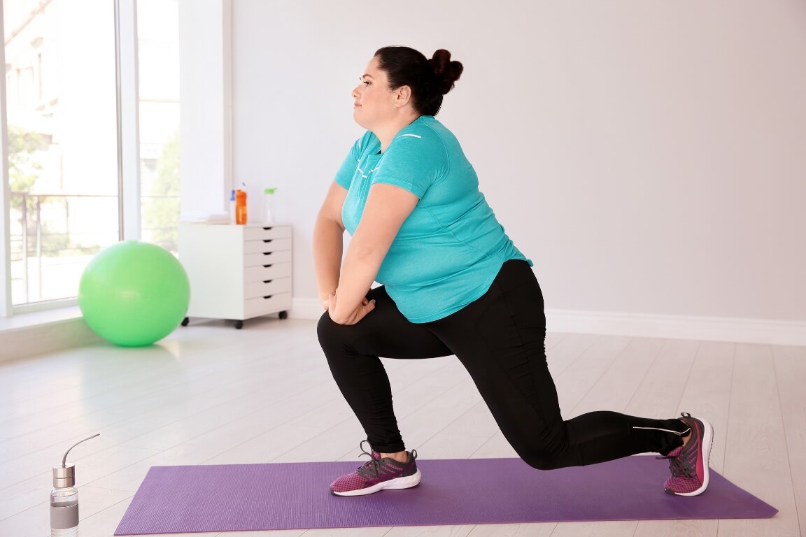 Overweight woman doing exercise on mat in gym 