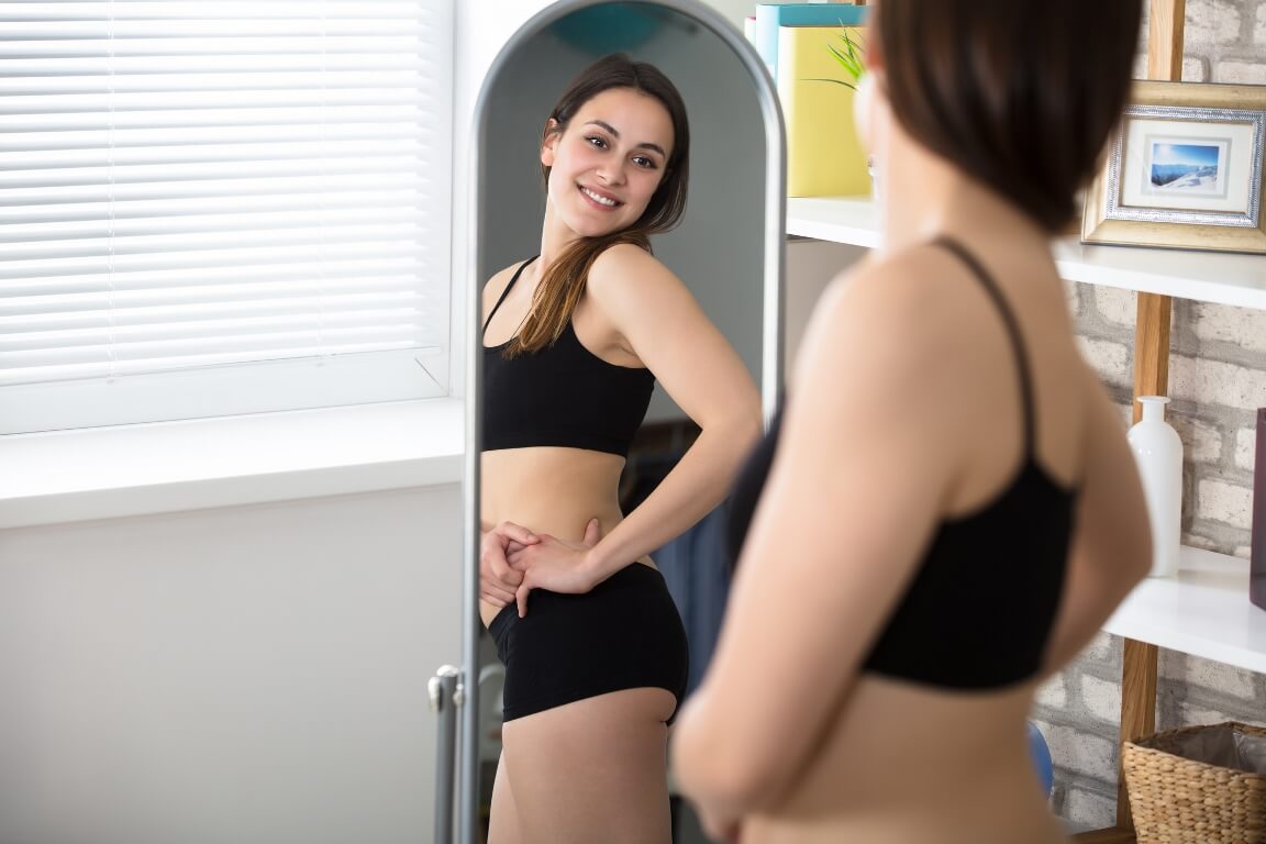 Smiling Slim Woman Looking At Her Reflection In Mirror